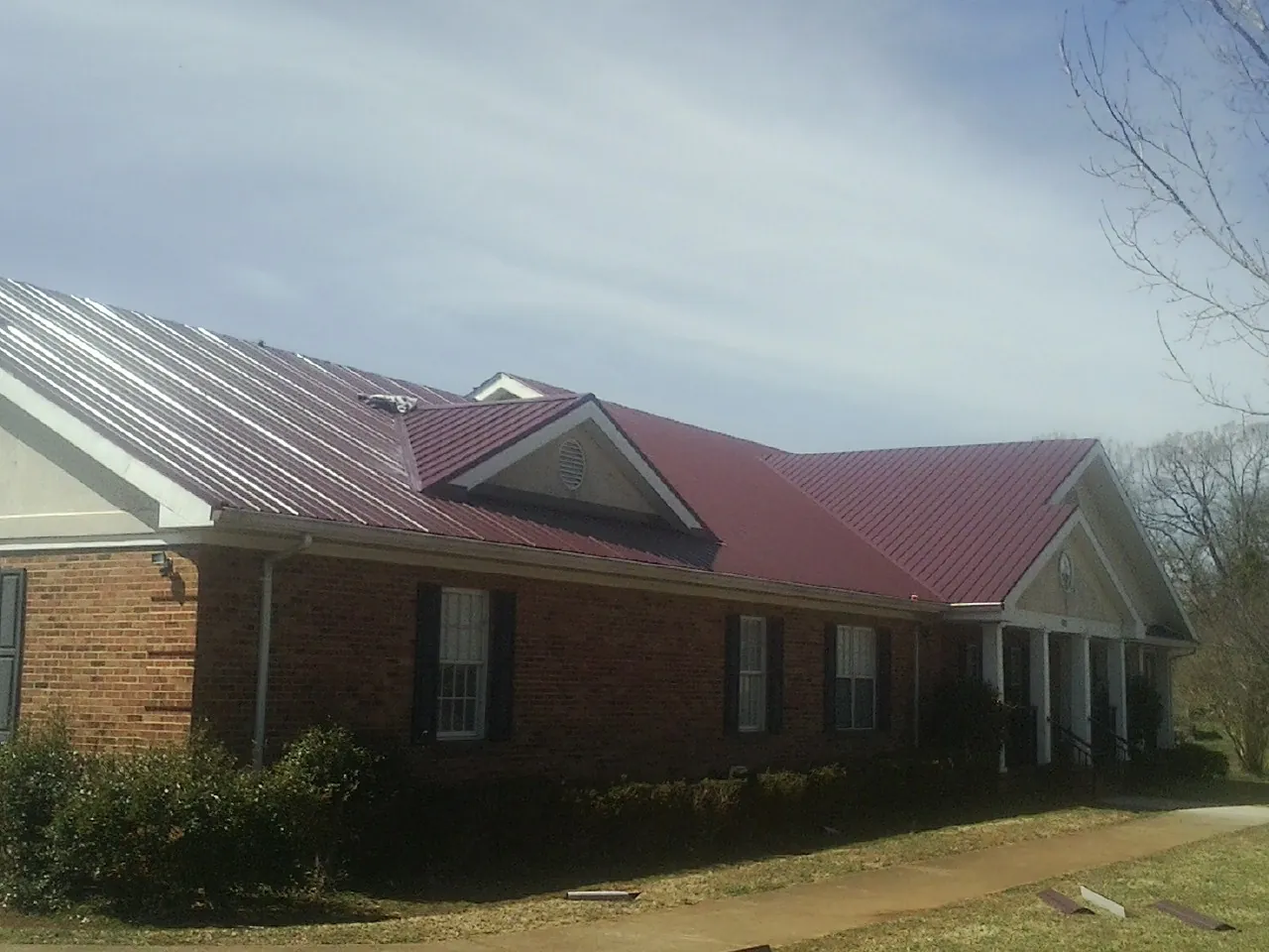 Red metal roof with gabled entries on a long brick building, from a Hail Damage Roof Repair job in Halifax