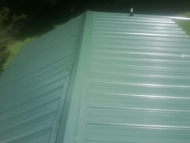 New green metal panels meeting at the ridge of a roof — Flat Roof Repair work by our crew in Halifax