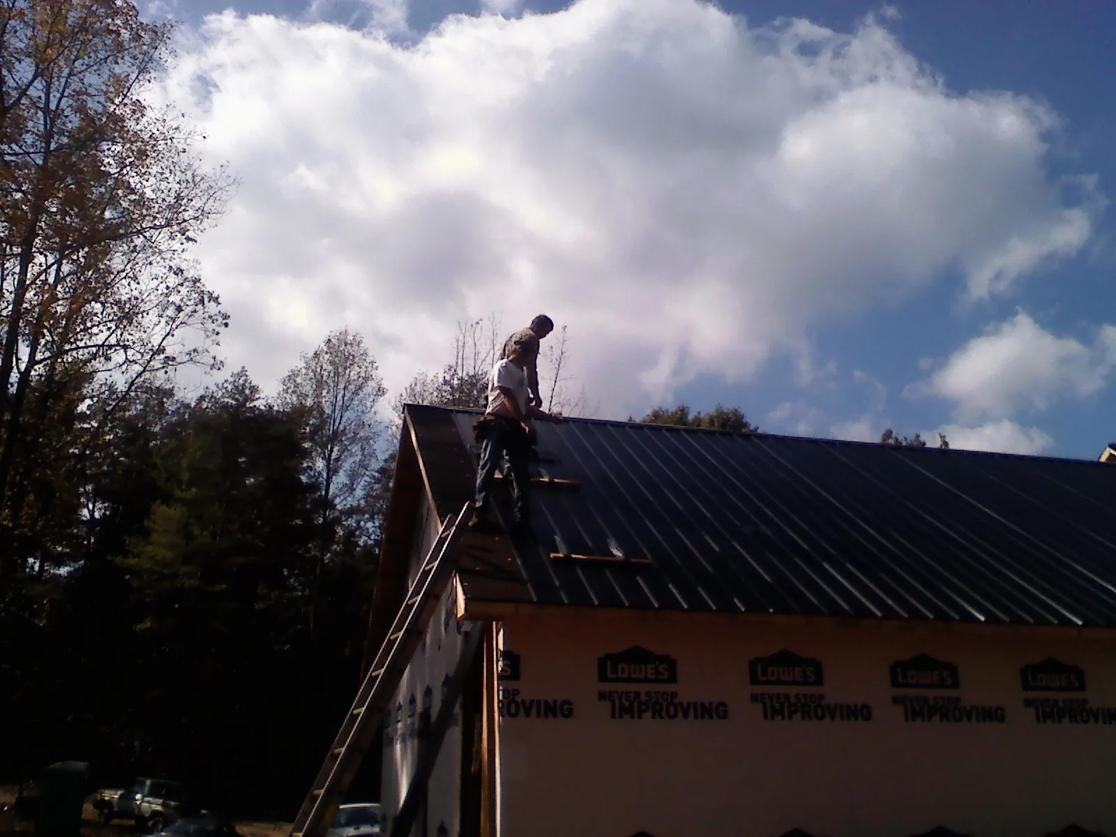 Roofer fastening dark metal panels high against a cloudy sky, from a Roof Inspection job in Halifax